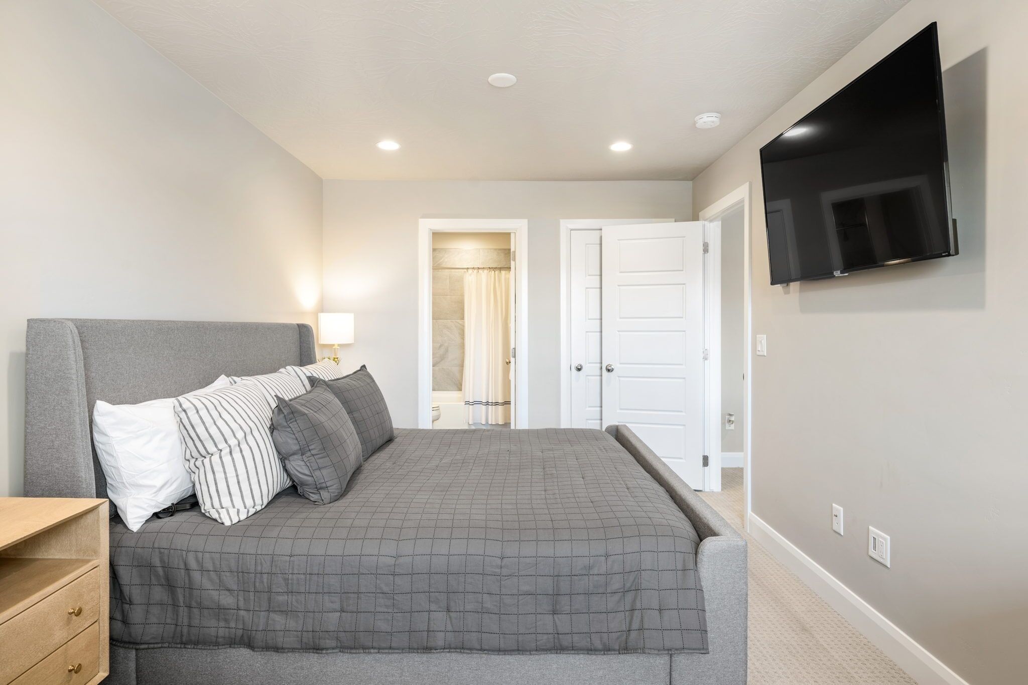 A bedroom with a bed, bedside table, lamp, and a TV mounted on the wall.