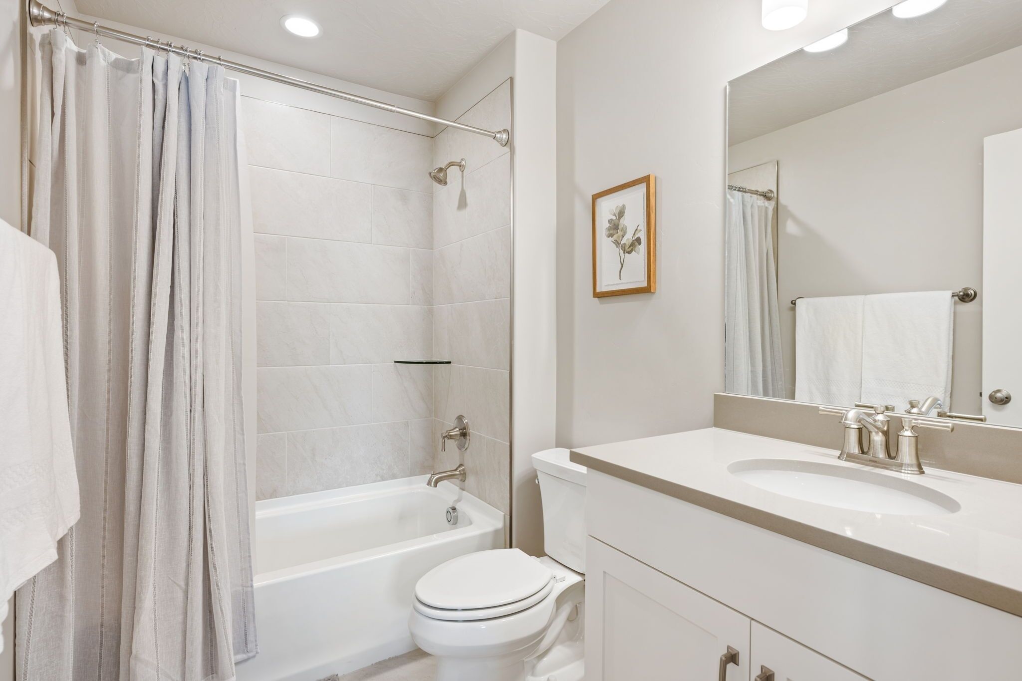 A modern bathroom with a bathtub, toilet, and vanity with a sink and mirror.