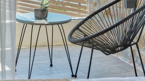 Een balkon met een stenen muur, een ronde tafel met een plant in pot, en een zwarte metalen stoel.