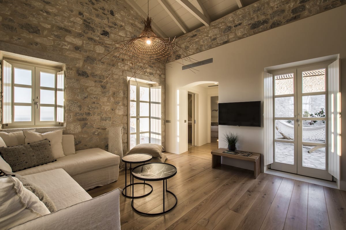 A spacious living room with a stone wall, a sofa, a round table, and a television.