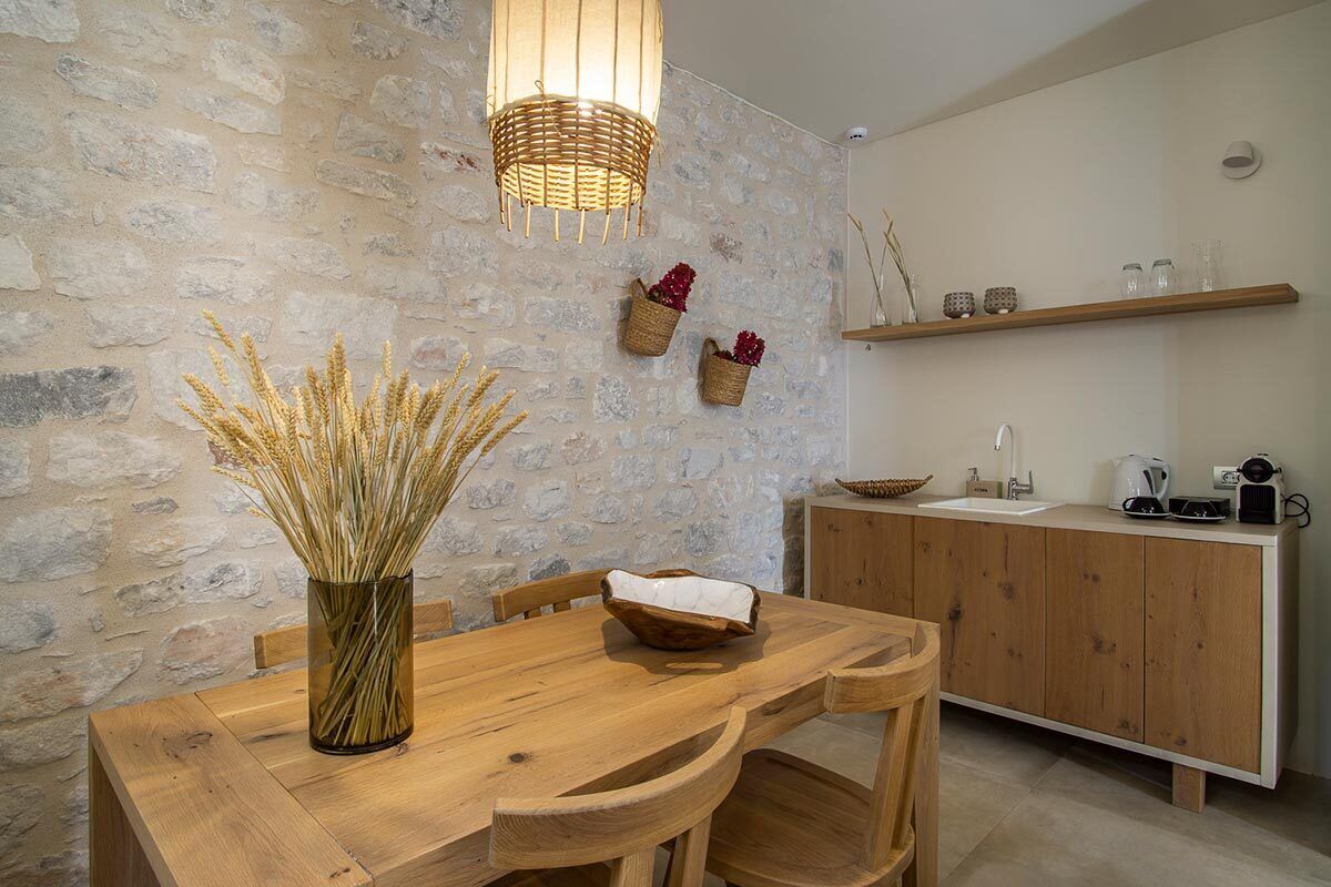 A rustic kitchen with a stone wall, wooden cabinets, and a wooden dining table with chairs.