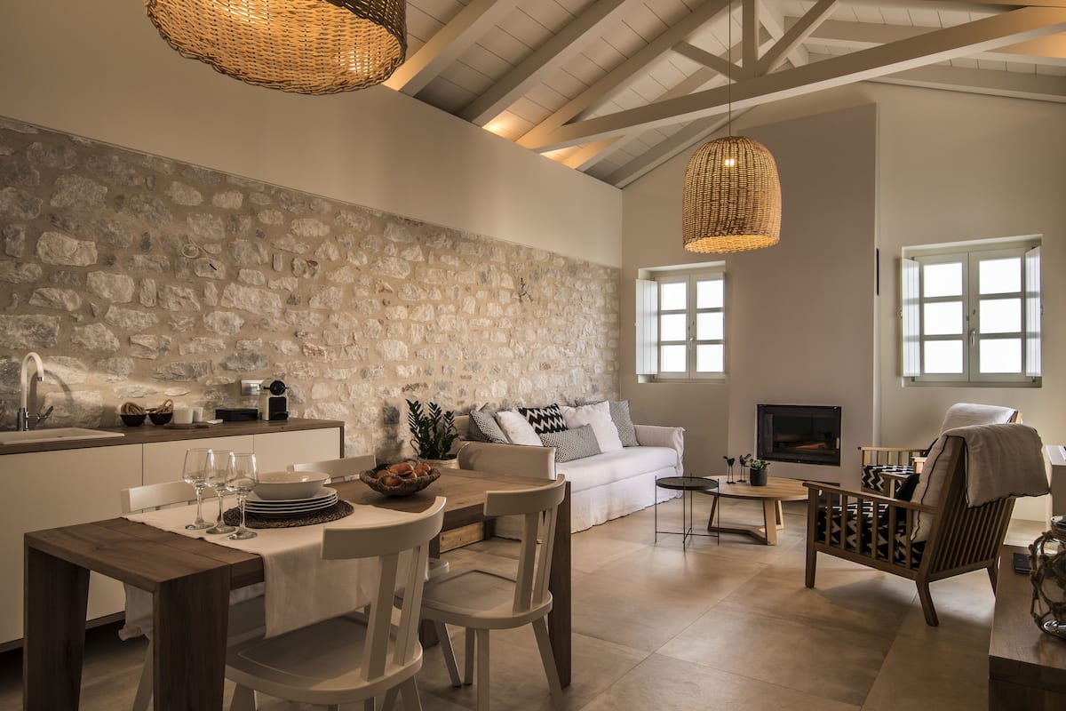 A modern kitchen with a stone wall, a dining area with a wooden table and chairs, a white sofa, and a fireplace.