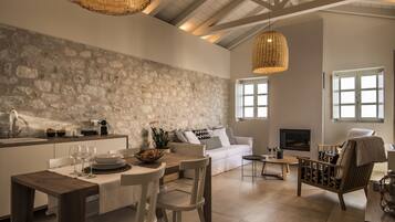 Uma cozinha moderna com parede de pedra, área de jantar com mesa e cadeiras de madeira, sofá branco e lareira.