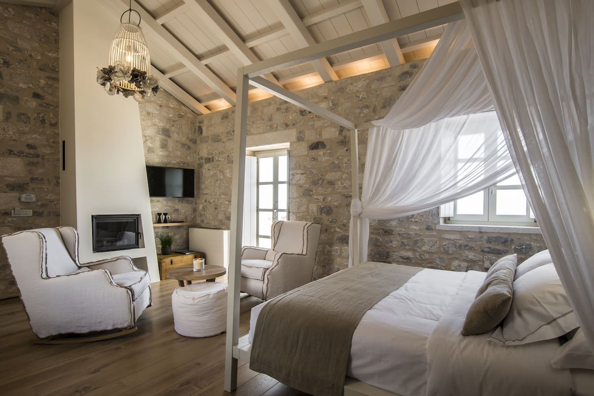 A bedroom with a stone wall, a TV, a bed, a chair, and a window with curtains.