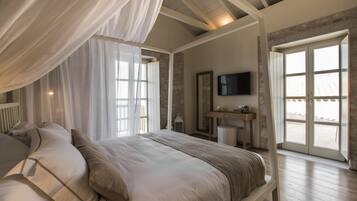 A bedroom with a large bed, a television, and a stone wall.