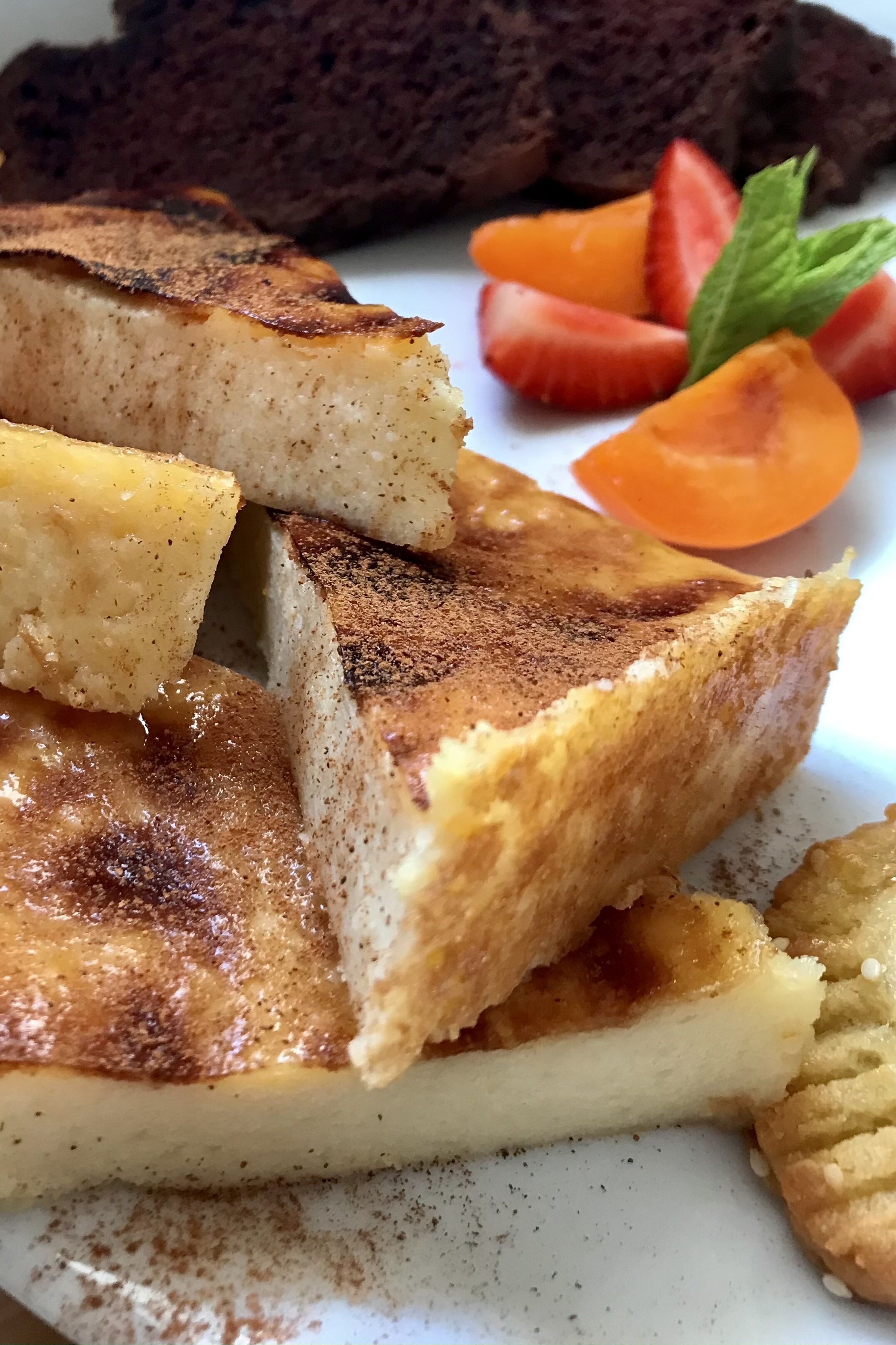 Un plato con rebanadas de un postre en capas, posiblemente un flan o una crema pastelera, acompañado de fresas frescas y una hoja de menta.