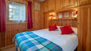 A wooden-paneled room with a bed, red pillows, a plaid blanket, and framed pictures on the wall. - Husky Cosy 2 Bed Alpine Apartment Views & Balcony (Saint-Gervais-les-Bains)