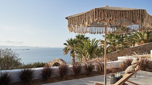 Un salon de plage agrémenté d’un parasol en macramé, de chaises longues et offrant une vue sur la mer.