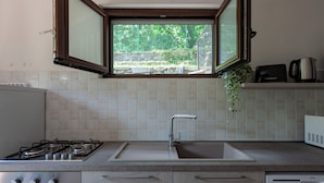 Een keuken met een gasfornuis, een spoelbak en een raam met uitzicht op groen.