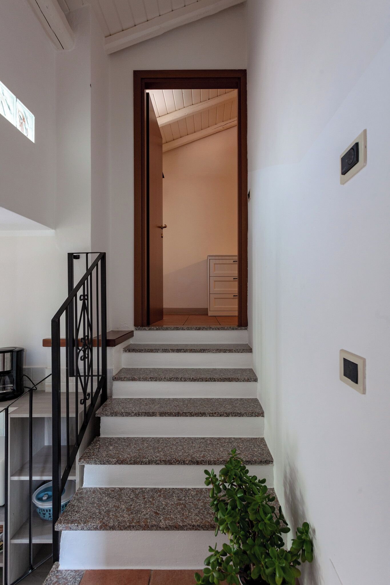 Un escalier aboutissant à une porte en bois, au sommet, qui donne sur une pièce comprenant un lit et une commode.