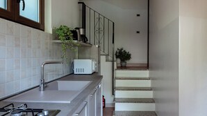 Een moderne keuken met een gasfornuis, spoelbak en witte kasten. Een trap leidt naar een ander niveau.
