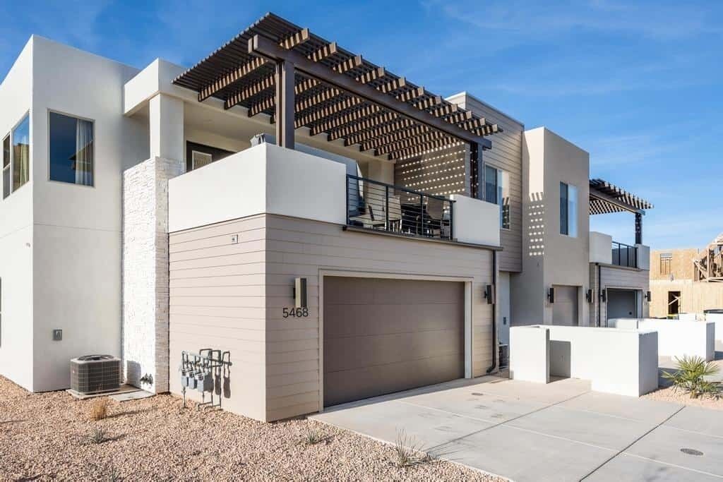 Un immeuble résidentiel moderne à deux étages, doté d’un garage, d’un patio couvert et offrant une vue sur un ciel dégagé.