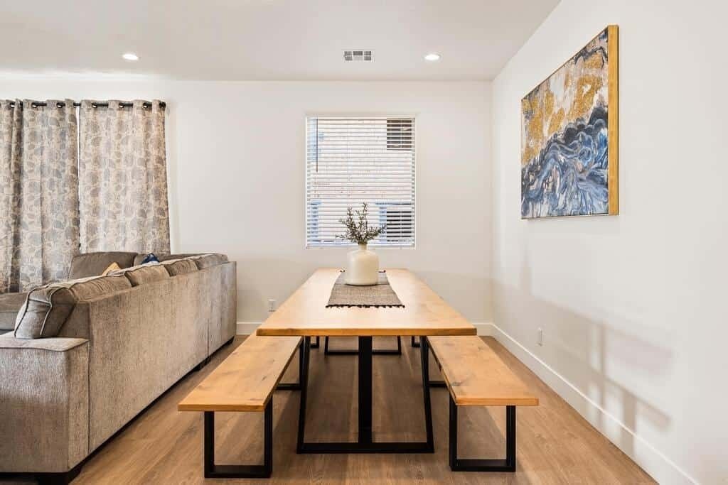 A modern living room with a wooden dining table, a sofa, and a window with blinds.