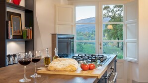 A kitchen with a large window, a gas stove, and a cutting board with bread and tomatoes. - Anticiana 8 (Lucca)
