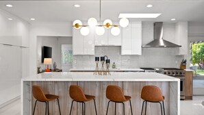 A modern kitchen with a large island, bar stools, a stainless steel range hood, and a view of the outdoors.