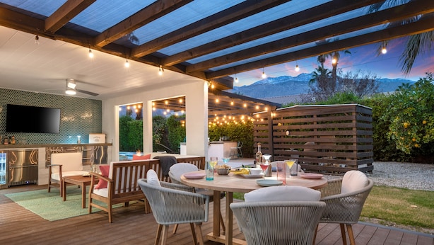 An outdoor patio with a wooden deck, wicker chairs, a round table, and string lights.