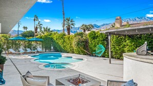 A pool area with lounge chairs, a fire pit, and a view of mountains.