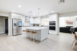 Uma cozinha moderna com ilha central, eletrodomésticos de aço inoxidável e banquetas.
