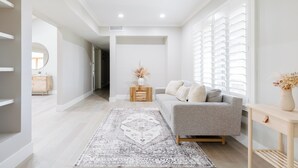 Een moderne woonkamer met een grijze bank, een vloerkleed met patroon en een houten bijzettafeltje met een vaas.