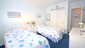 Une chambre avec deux lits, une table de chevet, une commode et une porte dotée d’un miroir.