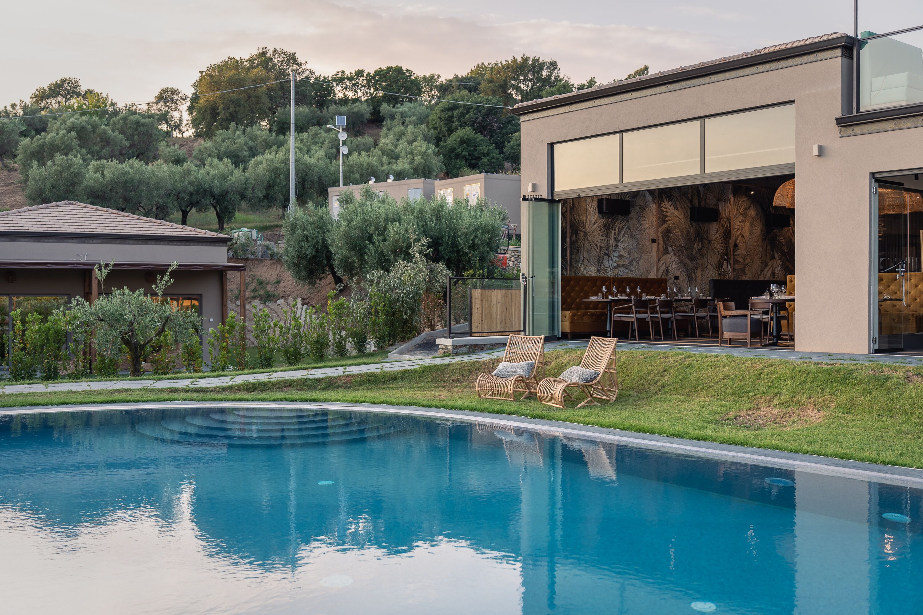 A modern house with a swimming pool, outdoor seating, and a view of the surrounding trees.
