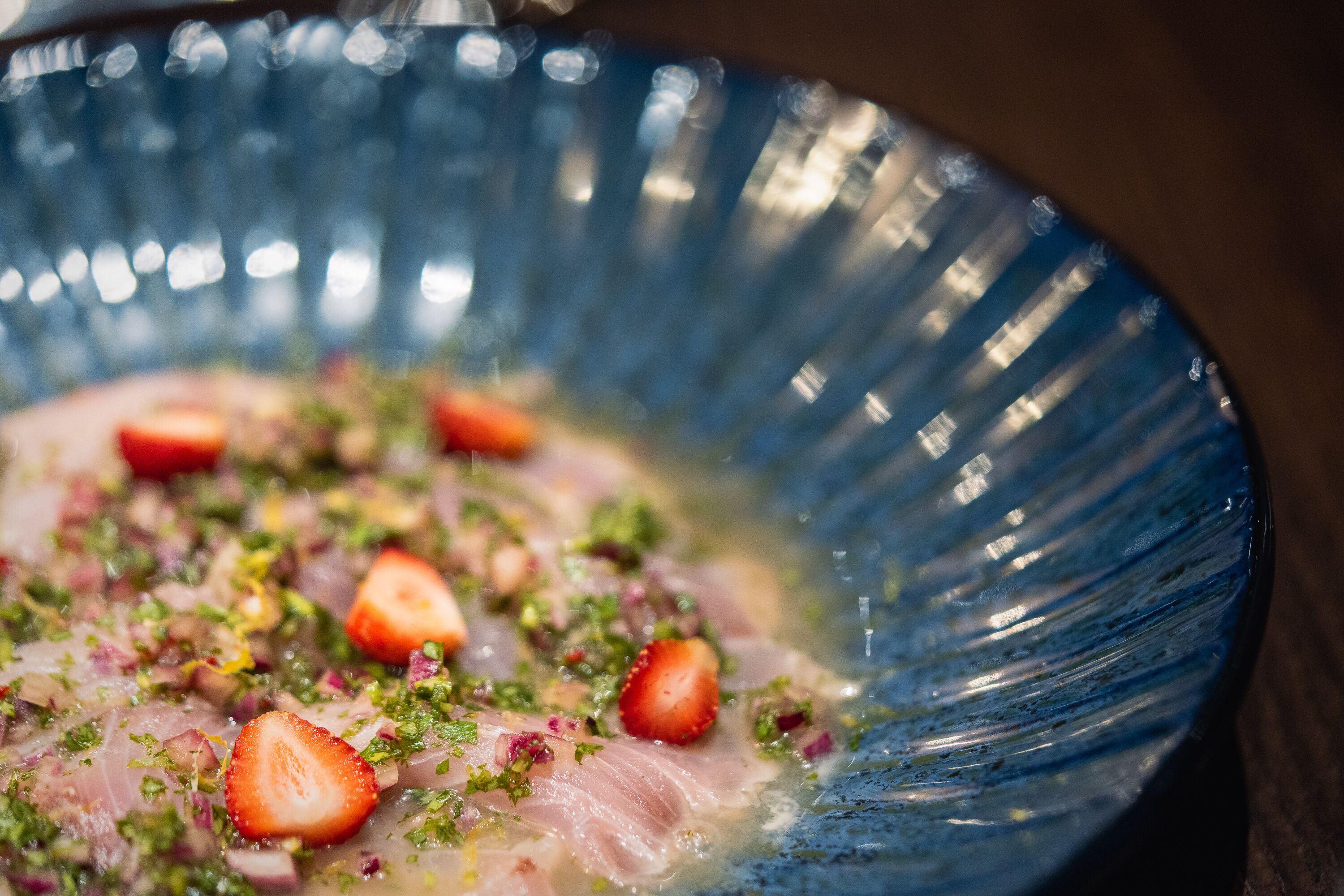 Un primo piano di un piatto di pesce con fragole e erbe aromatiche in una ciotola blu.