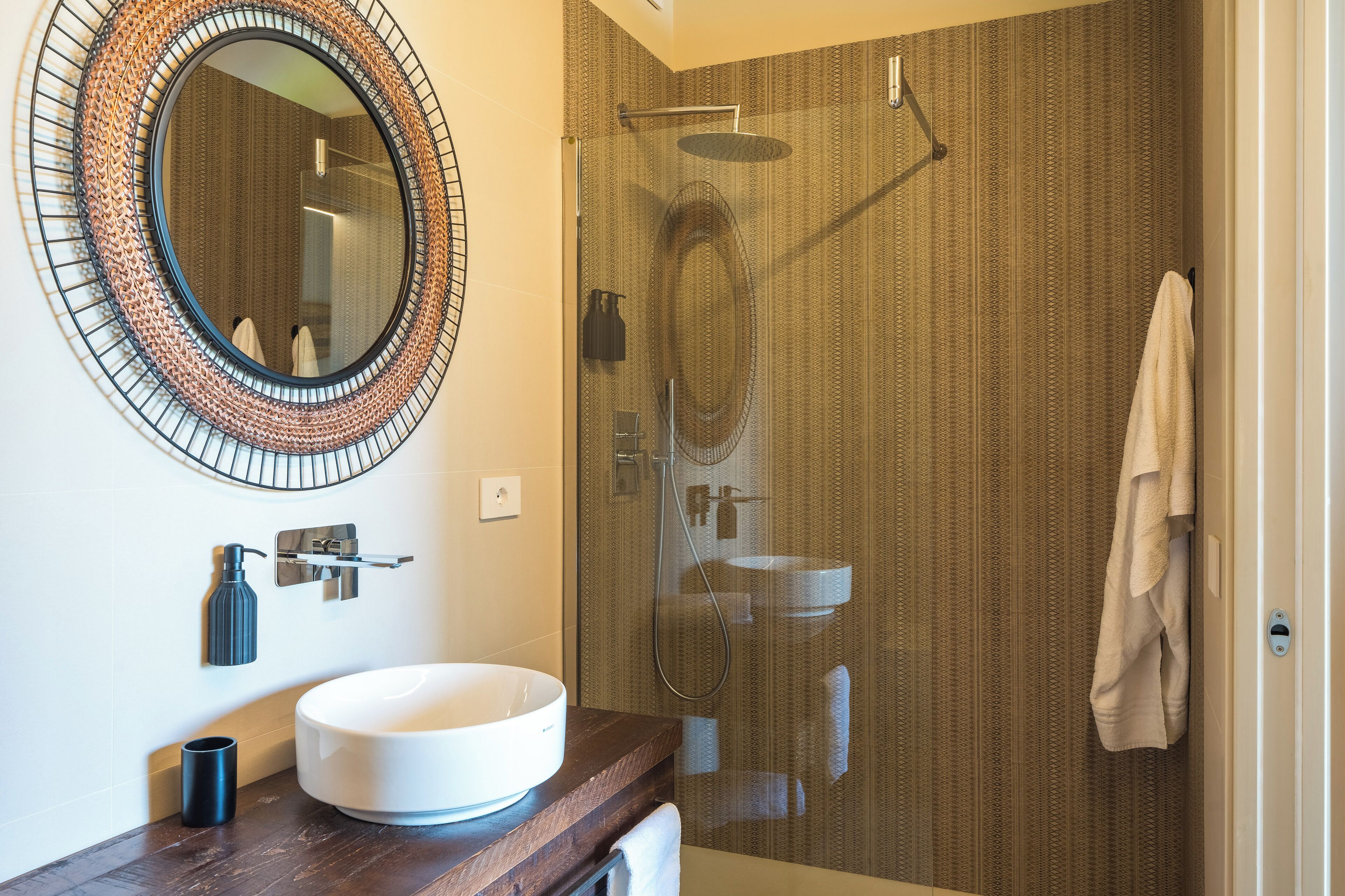 A modern bathroom with a round mirror, a white sink, and a glass-enclosed shower.