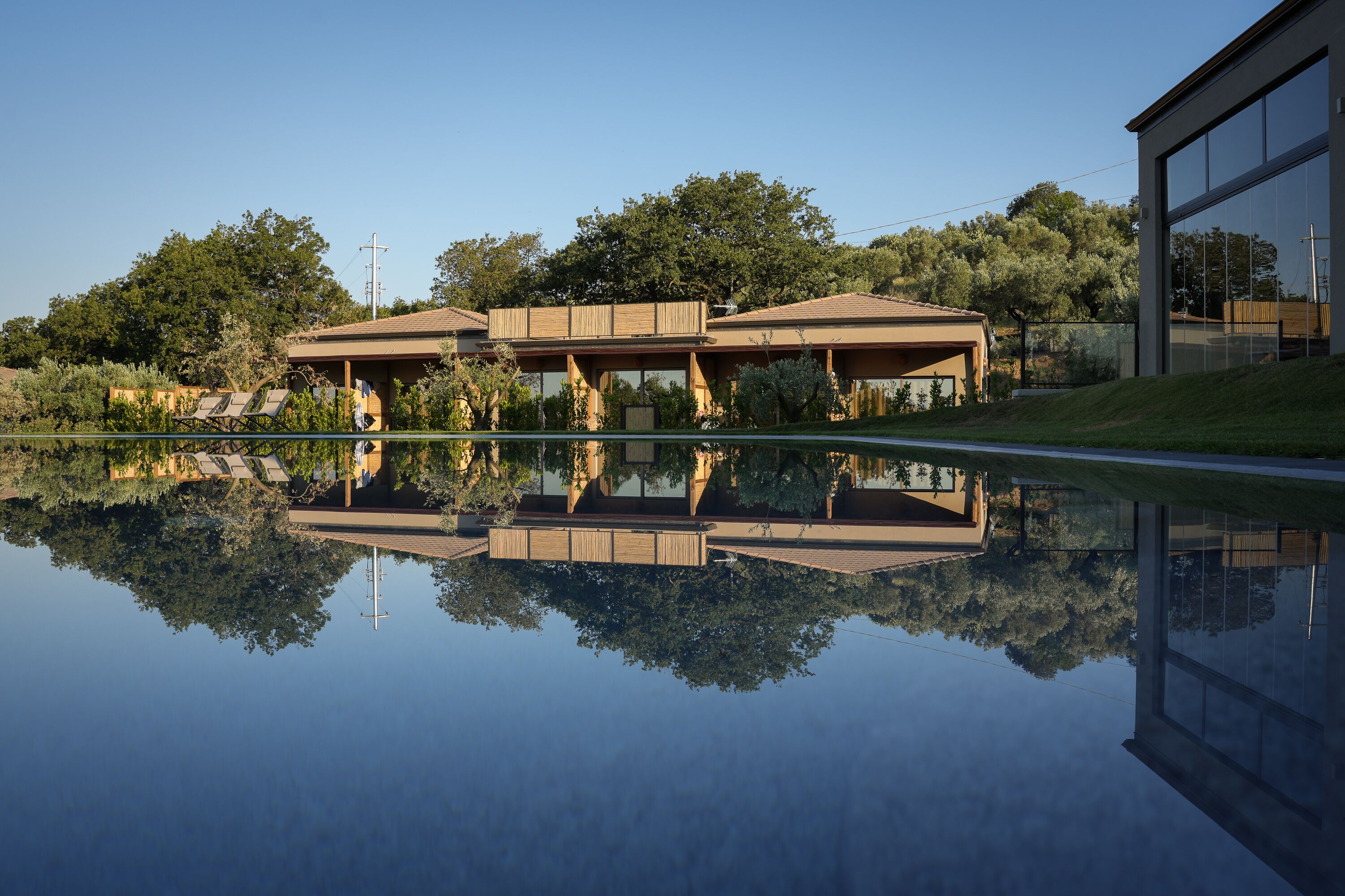 A modern building with a reflective pool in front, surrounded by trees and a clear sky.
