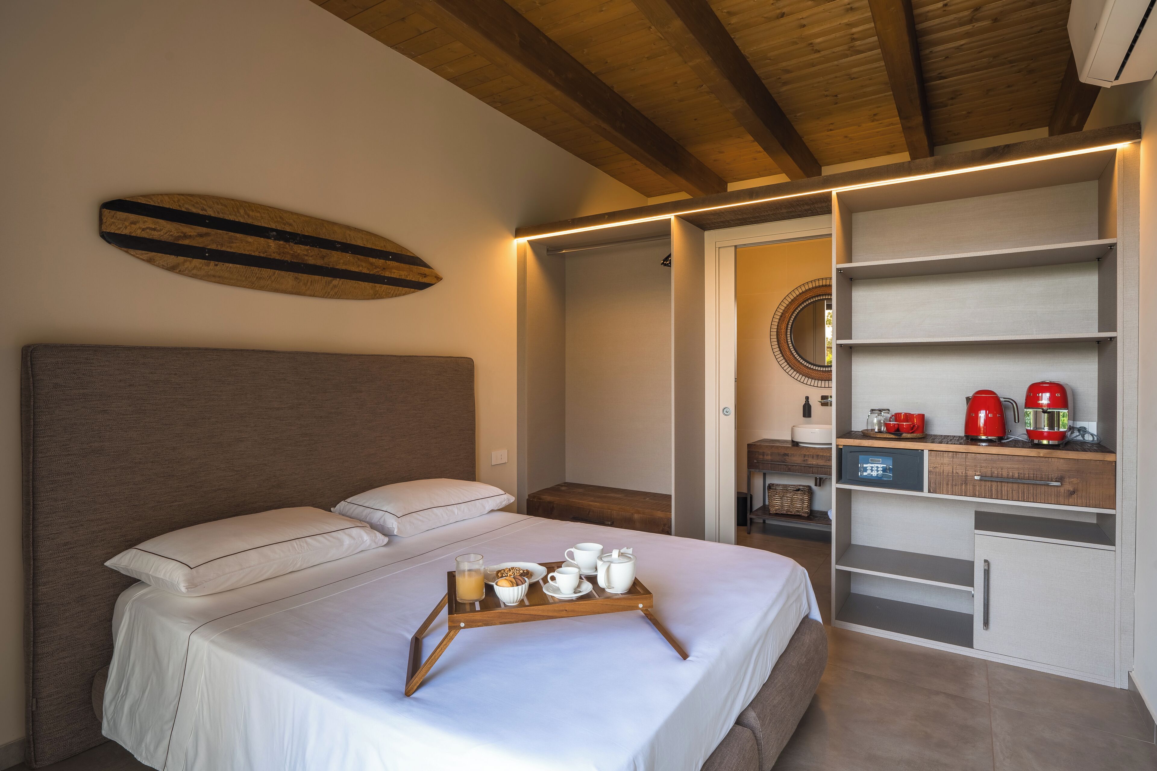Una cama bien hecha con una bandeja de desayuno, un cabecero de madera y una estantería moderna con un hervidor rojo.