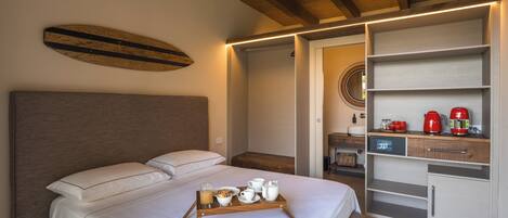 Una cama bien hecha con una bandeja de desayuno, un cabecero de madera y una estantería moderna con un hervidor rojo.