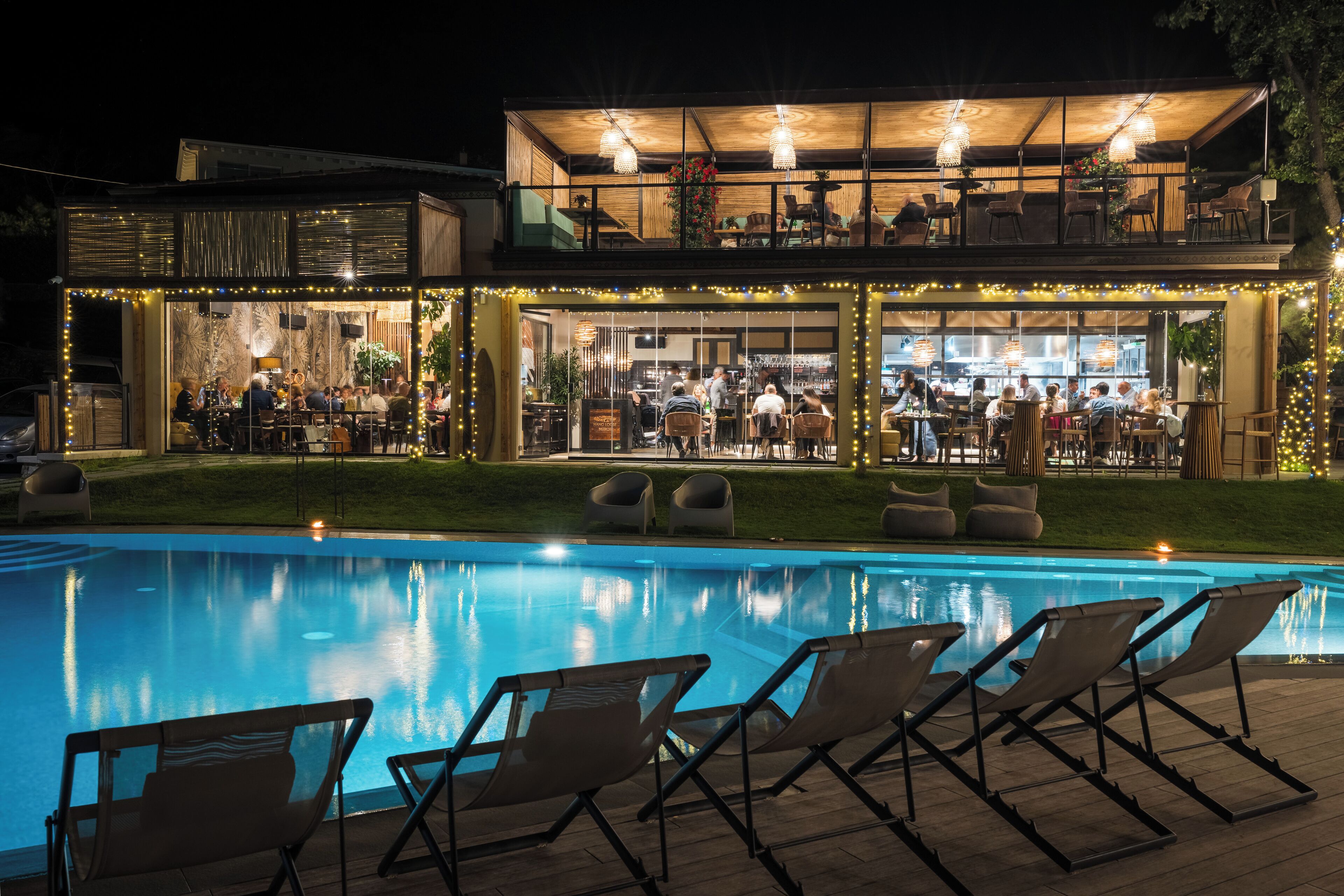 Ein Poolbereich mit Liegestühlen, eine Bar mit Gästen und ein Restaurant mit Außenbereich.