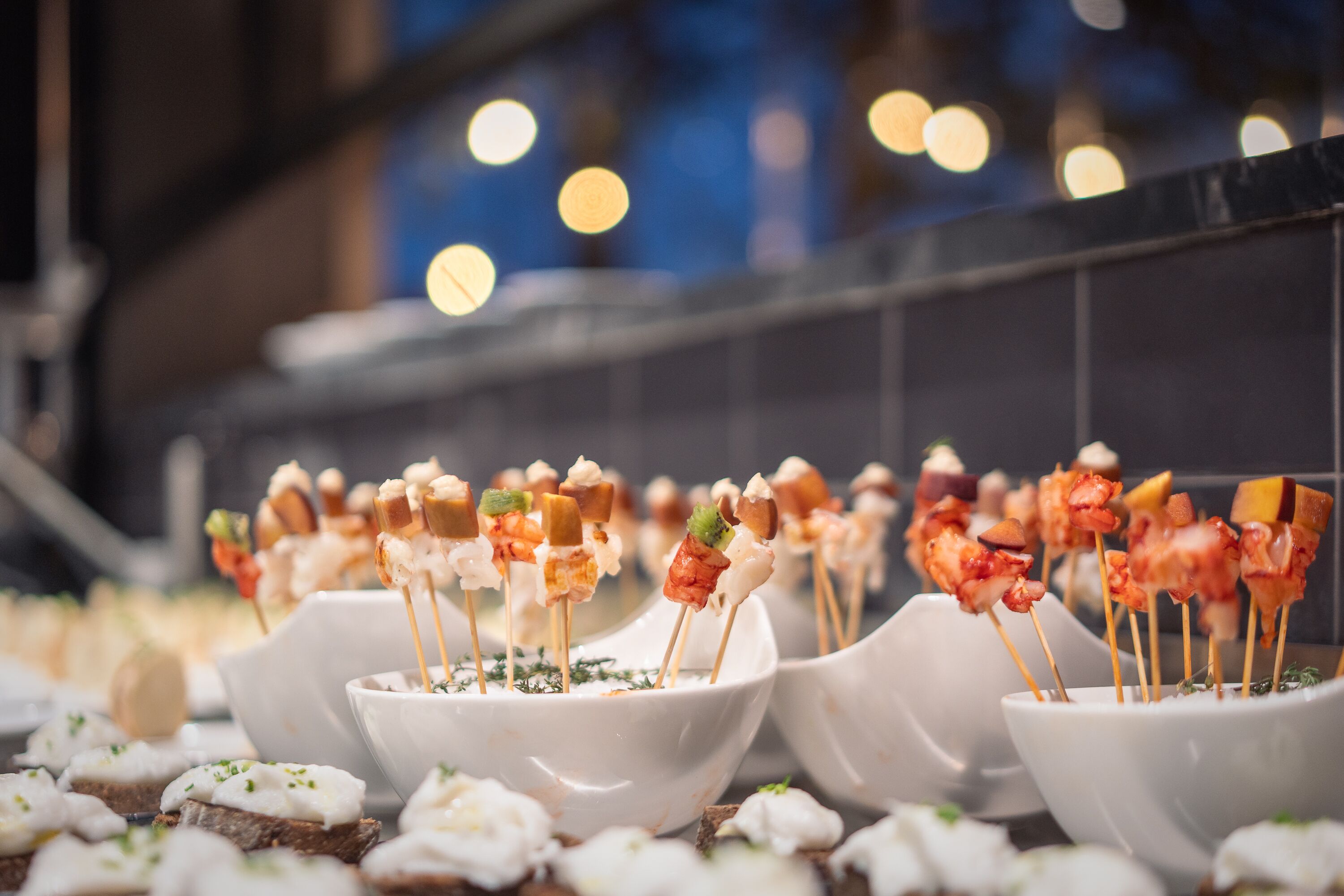 Una serie de cuencos blancos con brochetas de comida, probablemente aperitivos, dispuestas sobre una mesa.