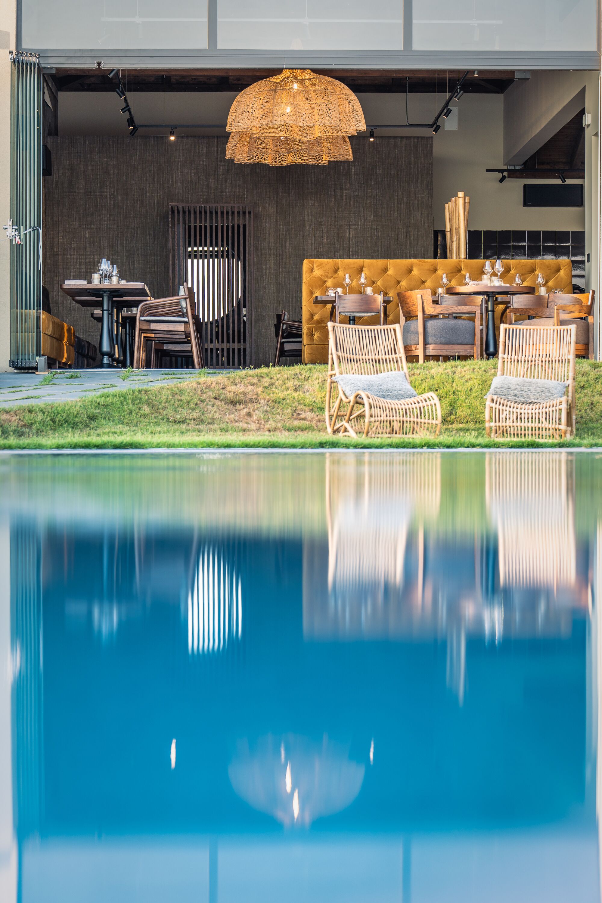 A poolside area with wicker chairs, a table with chairs, and a large woven light fixture.