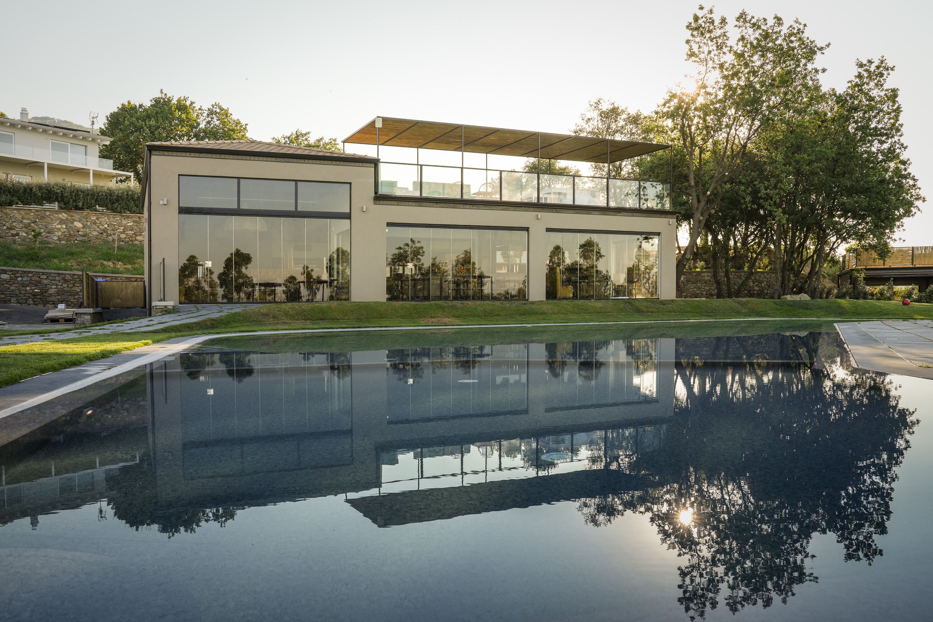 Una casa moderna con ampie vetrate, una piscina e un muro in pietra.