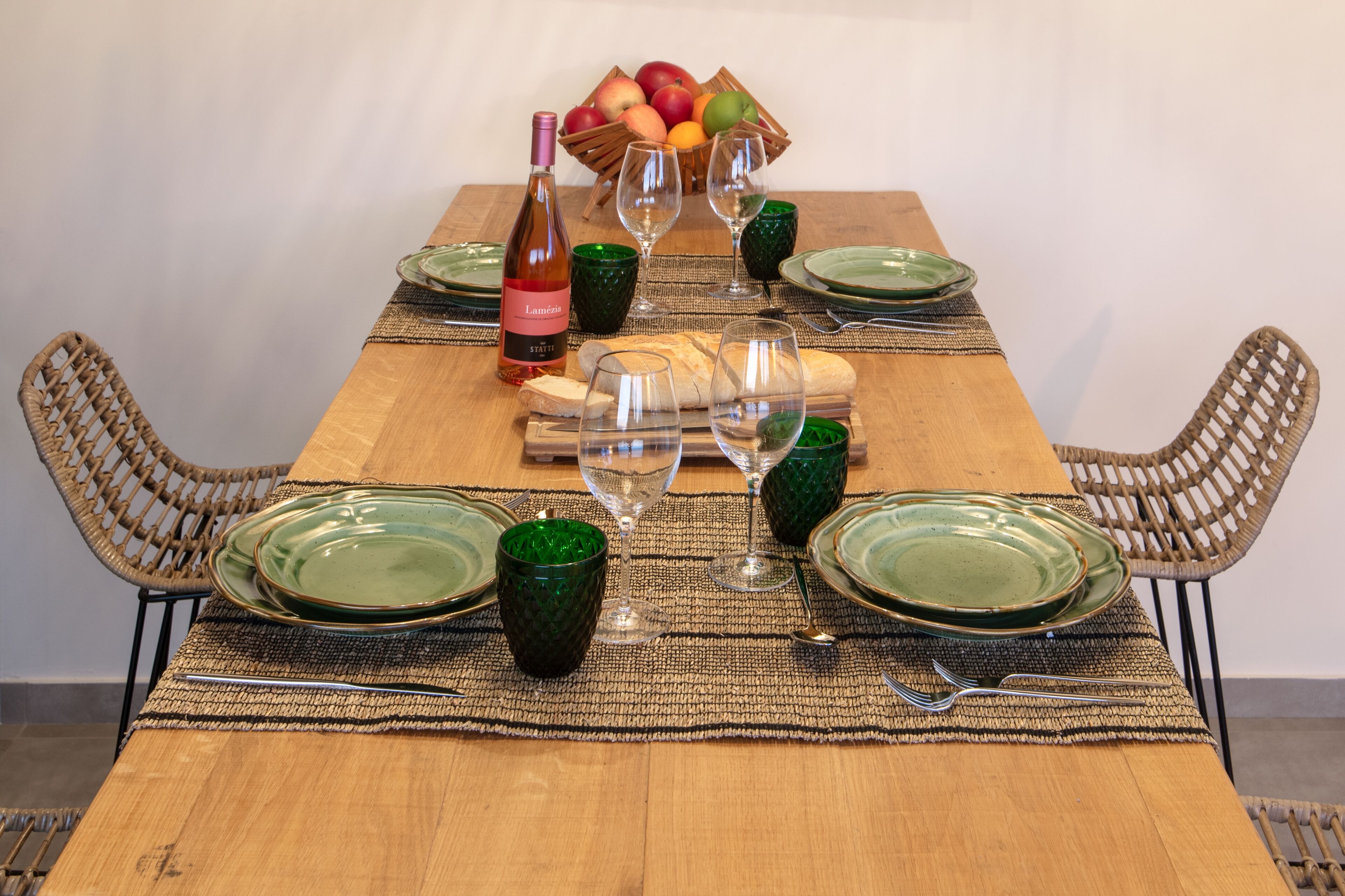 A wooden dining table set with green plates, wine glasses, and a bottle of wine.