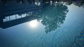 Un bâtiment avec une piscine dont la surface est réfléchissante et un arbre qui se reflète dans l’eau.