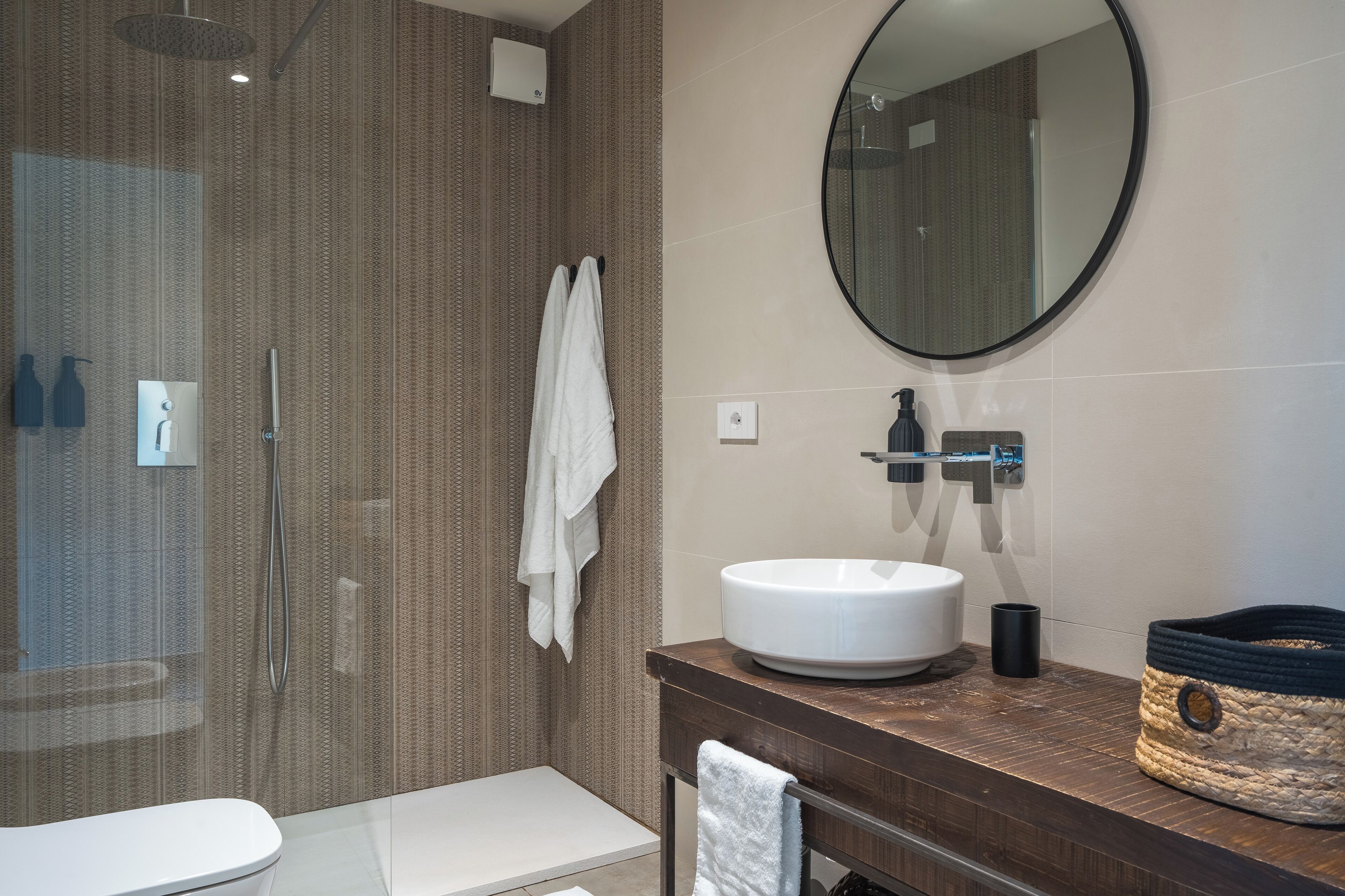 A modern bathroom with a glass-enclosed shower, a white sink, and a round mirror.