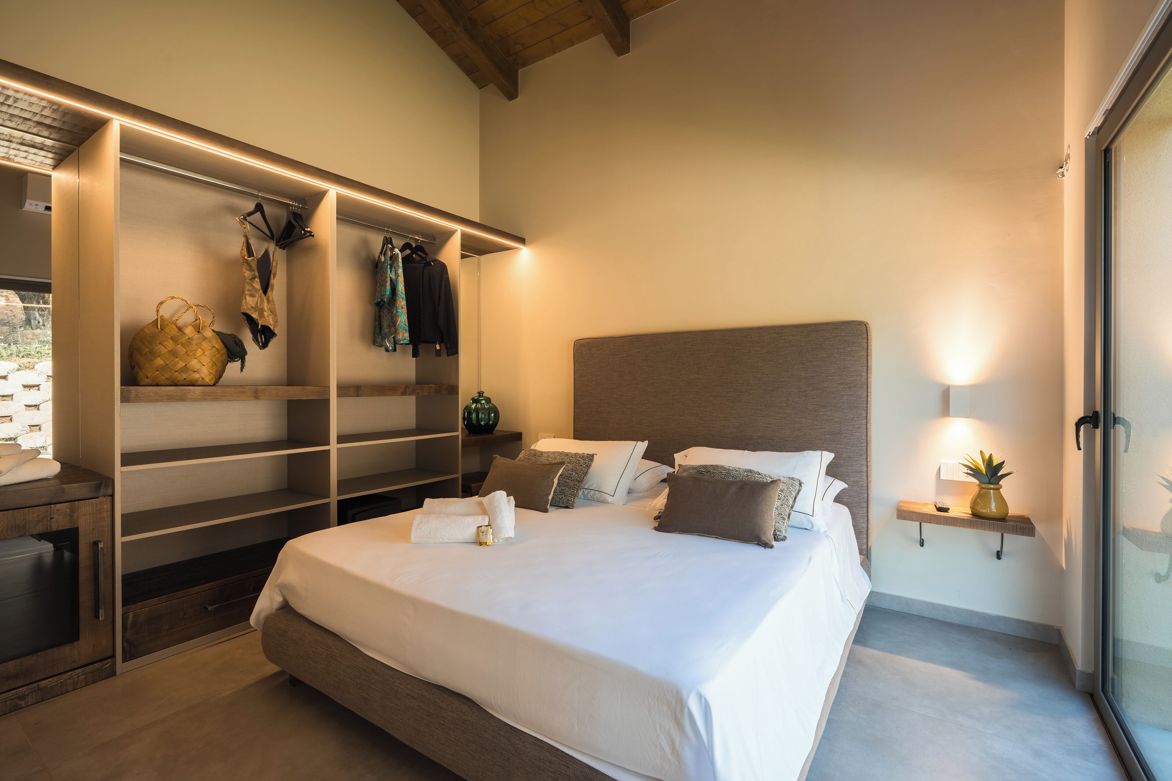 A modern bedroom with a large bed, built-in wardrobe, and a bedside table with a lamp.