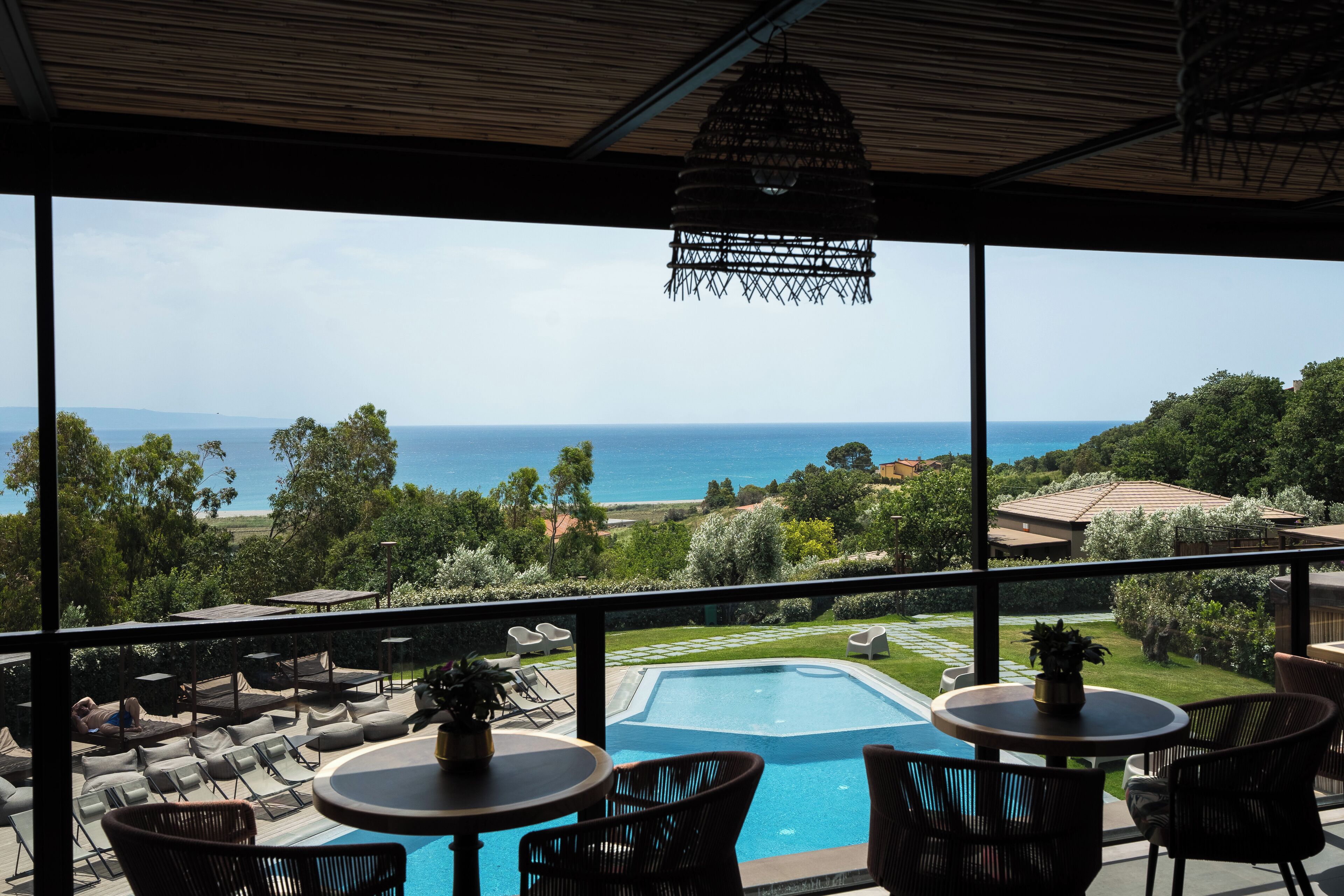 A balcony with a view of the sea, a pool, and outdoor seating.