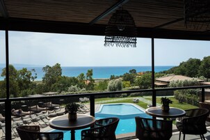 A balcony with a view of the sea, a pool, and outdoor seating.