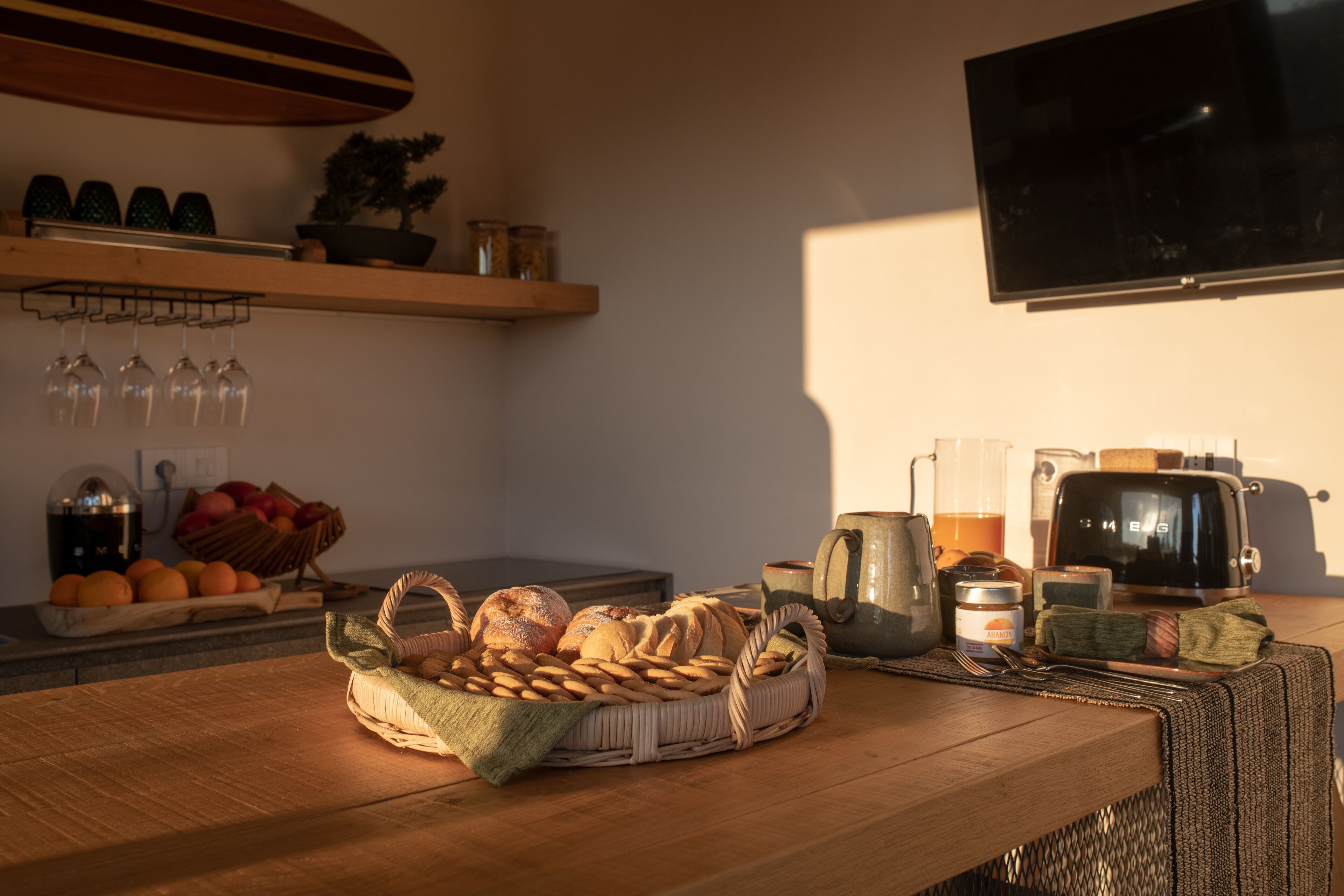 Une cuisine avec une table en bois, un panier de pain, un grille-pain et un téléviseur fixé au mur.