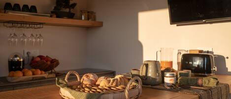 A kitchen with a wooden table, a basket of bread, a toaster, and a TV mounted on the wall.