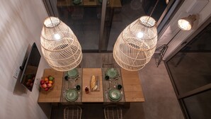 A dining area with a wooden table set for four, two wicker pendant lights, and a fruit bowl on the wall.