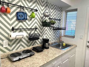 A kitchen with a chevron-patterned backsplash, a coffee maker, a sink, and a window with a view.