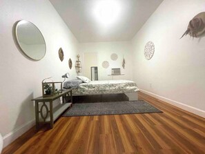 Een slaapkamer met een bed, nachtkastje, spiegel en decoratieve wanddecoratie.