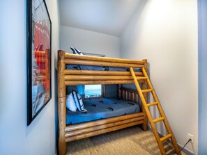 A bunk bed with a ladder, a framed picture on the wall, and a window with blinds.