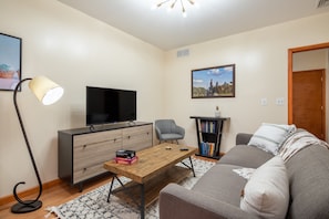 A living room with a sofa, a coffee table, a TV, a bookshelf, and a lamp.