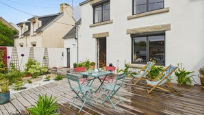 A wooden deck with outdoor furniture, potted plants, and a white building with large windows. - House for 6 rated 3* - Terrace - Guilvinec (Le Guilvinec)