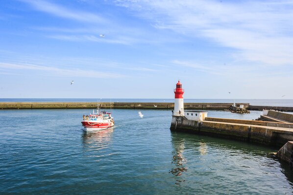 Ein rotes und weißes Boot liegt an einem Leuchtturm an einem ruhigen Meer.