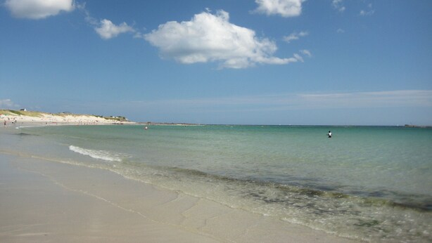 Een strand met helder water, een zandstrand en enkele mensen in de verte.